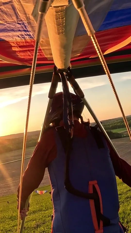 A pilot beneath a Falcon hang-glider wing in warm evening light